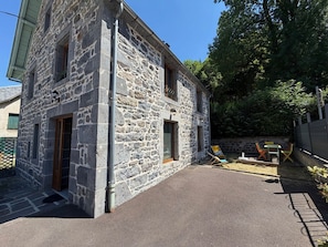 A stone building with a paved courtyard, outdoor seating, and a view of trees. - Charming house, parking, city center - 8 guests (Mont-Dore)