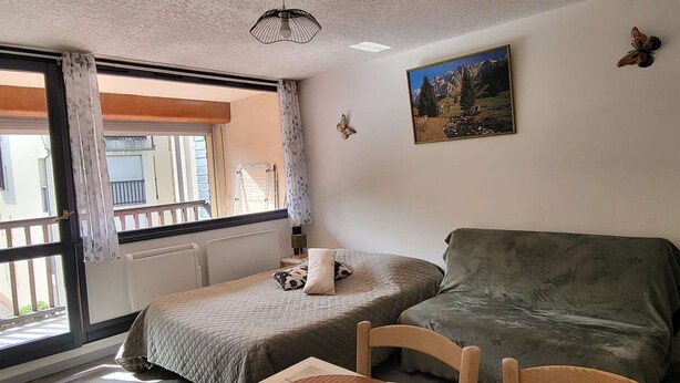 Una habitación con dos camas, una mesa, una silla, un cuadro y una ventana con vistas a edificios.