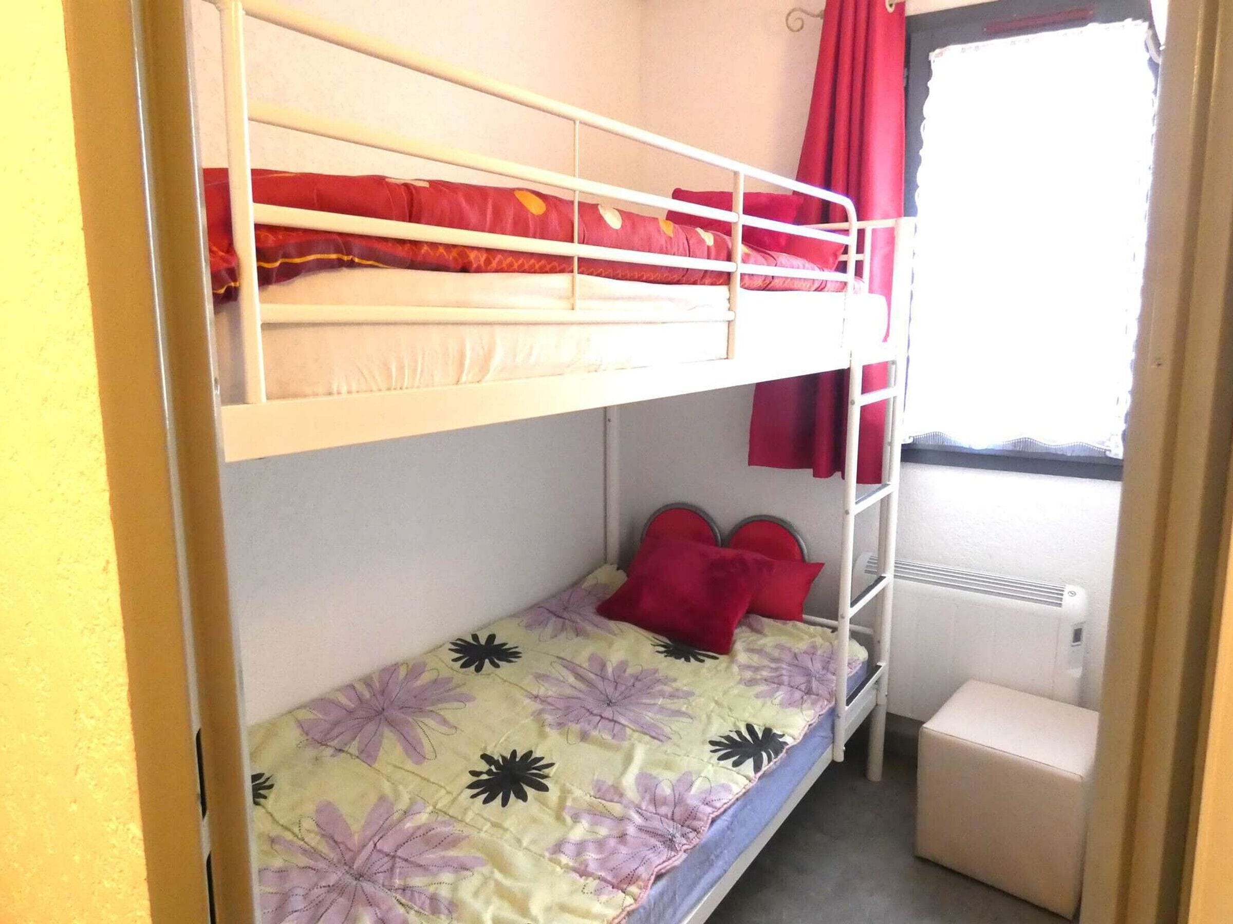 Quarto com beliche, janela, radiador e uma pequena mesa de cabeceira.