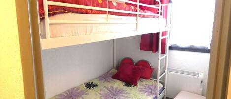 Quarto com beliche, janela, radiador e uma pequena mesa de cabeceira.