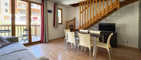 A living room with a wooden staircase, a dining area with chairs, a sofa, and a television.