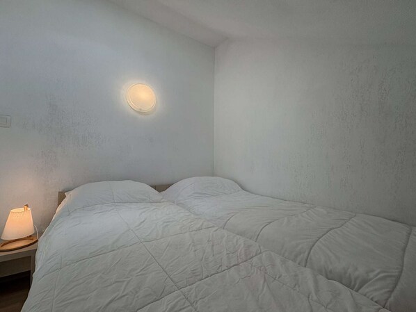 Een enkel bed met een witte deken in een kamer met een gestructureerde muur en een ronde wandlamp.