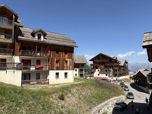 A traditional wooden chalet-style building with balconies, a visible sign indicating a sale, and a clear view of the surrounding mountainous landscape. - Cozy duplex near slopes - 8 guests (Les Orres)