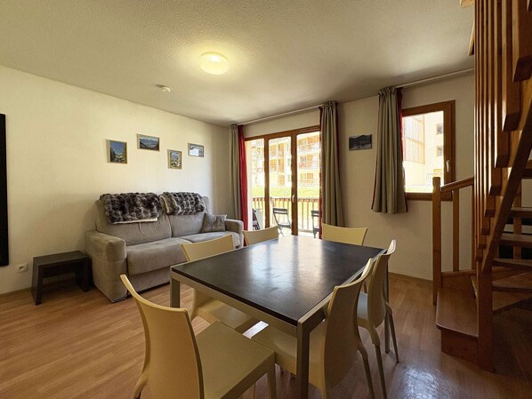 A living room with a sofa, a dining table with chairs, a staircase, and a view of the outside. - Cozy duplex near slopes - 8 guests (Les Orres)