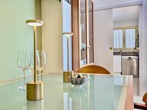 A modern dining area with a glass table, two wine glasses, a decorative bowl, and a cabinet with glass doors. - Apartment with jacuzzi - 6 guests (Tossa de Mar)