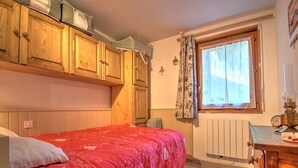 Een slaapkamer met een bed, houten kasten, een radiator en een raam met gordijnen.
