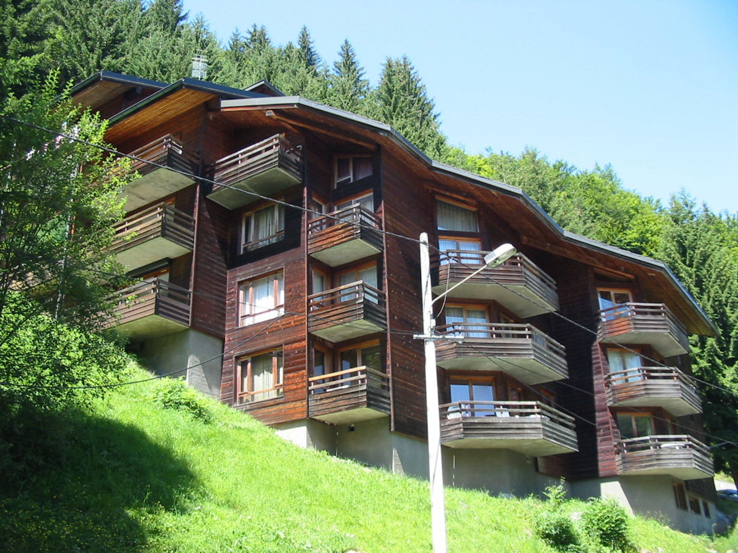 Un edificio de madera de varios pisos con balcones, rodeado de vegetación.