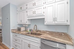 A kitchen with white cabinets, a marble countertop, a sink, and a dishwasher. - Shipwatch Pointe 1-319G (Myrtle Beach)