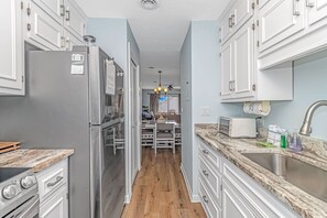 A modern kitchen with stainless steel appliances, white cabinetry, and a marble countertop. - Shipwatch Pointe 1-319G (Myrtle Beach)