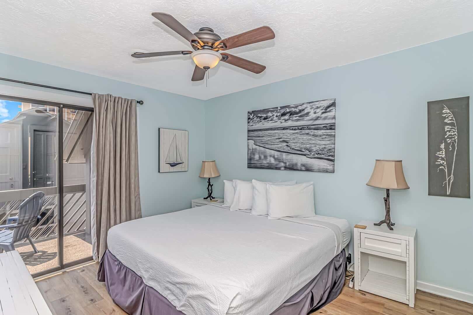 Um quarto com uma cama, um ventilador de teto, uma janela com cortinas e obras de arte nas paredes.