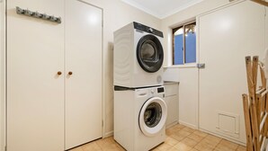 A compact laundry room with a front-loading washer and dryer, a small window, and a wooden rack. - The Burwood Cottage Comfort & Convenience (Burwood)