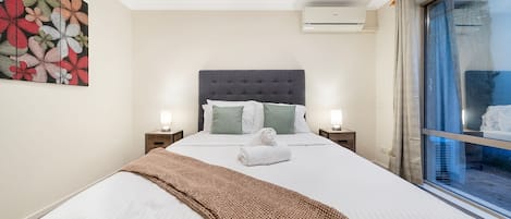 Een hotelkamer met een bed, twee nachtkastjes, een wandairconditioner en een raam met gordijnen.