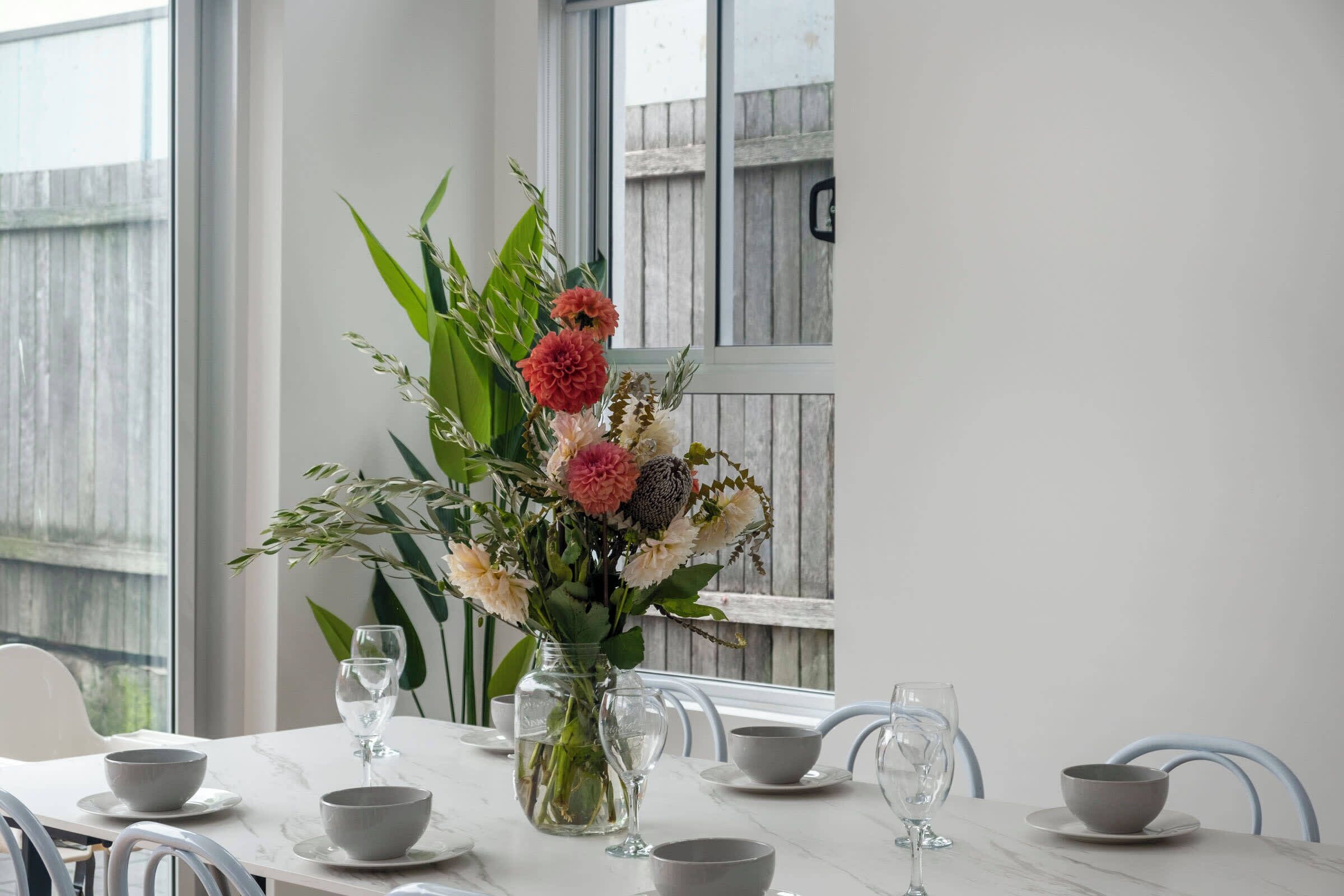 Une table à manger ornée d’un vase de fleurs, de verres transparents et de bols gris.