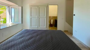 Een slaapkamer met een bed, een raam, een kledingkast en een badkamer die door een geopende deur zichtbaar is.