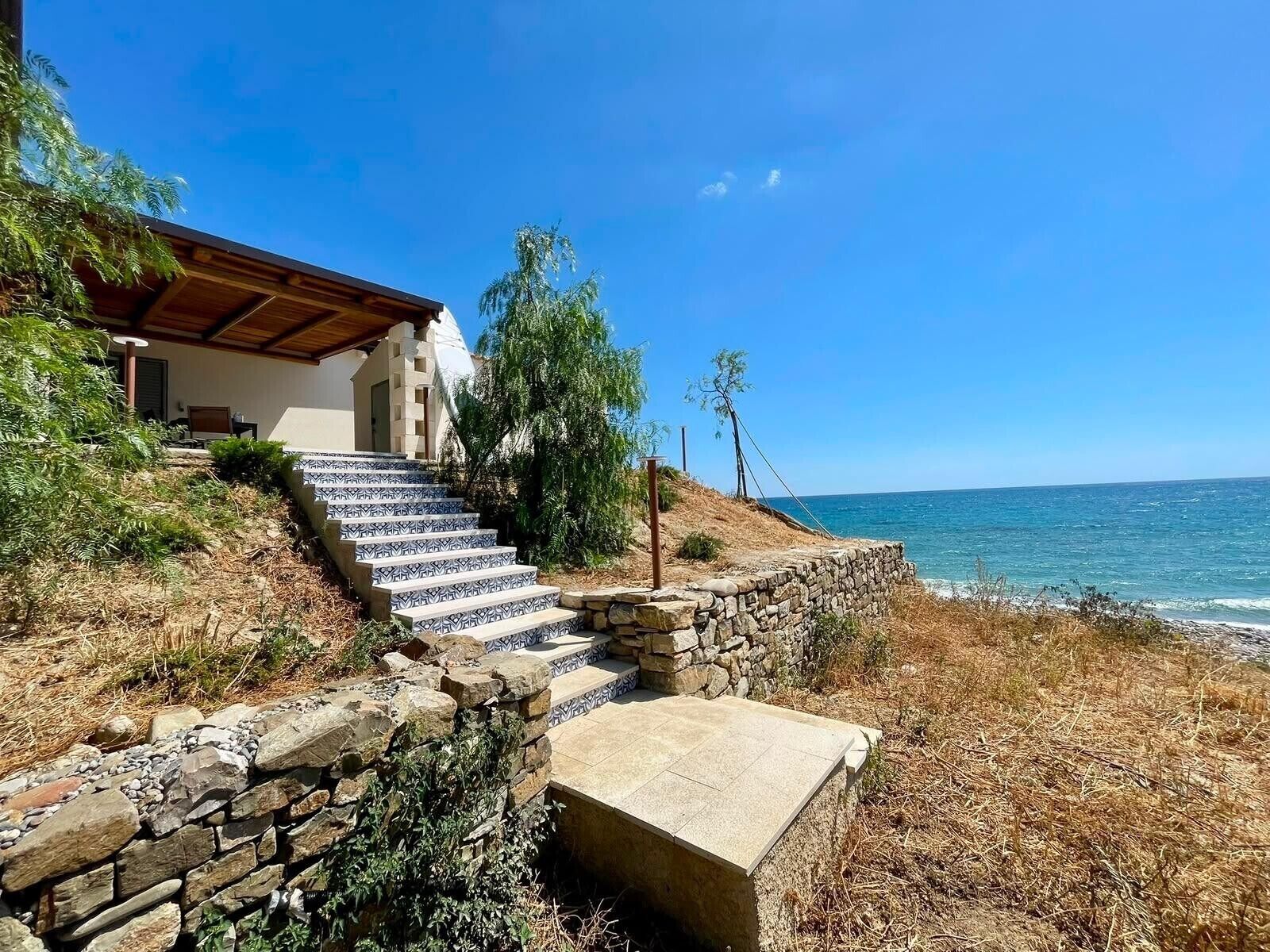 Una proprietà costiera con una scala in pietra che conduce a una casa con tetto in legno, con vista sul mare.