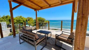 Ein Sitzbereich im Freien mit einer Holzpergola, Blick auf das Meer und einem Strand im Hintergrund.