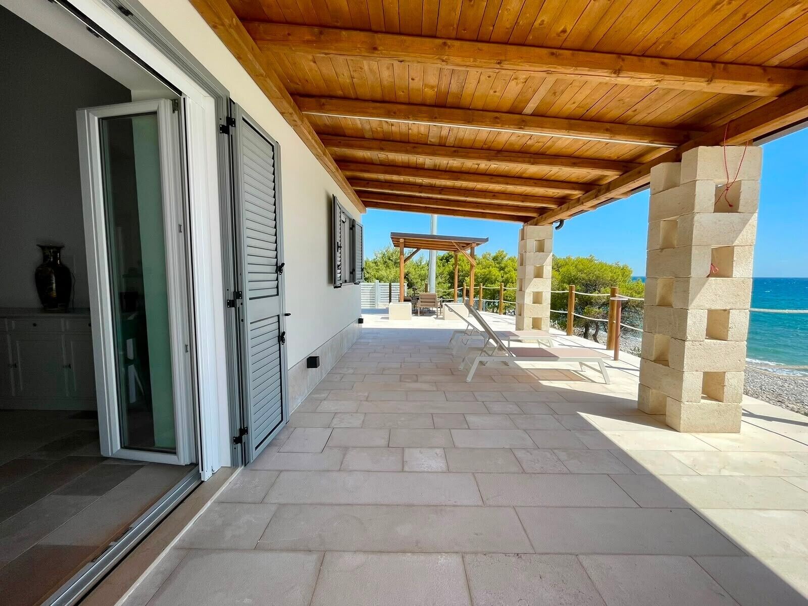 Un espace extérieur abrité, avec vue sur la mer, doté d’un plafond en bois et d’un pilier en pierre.