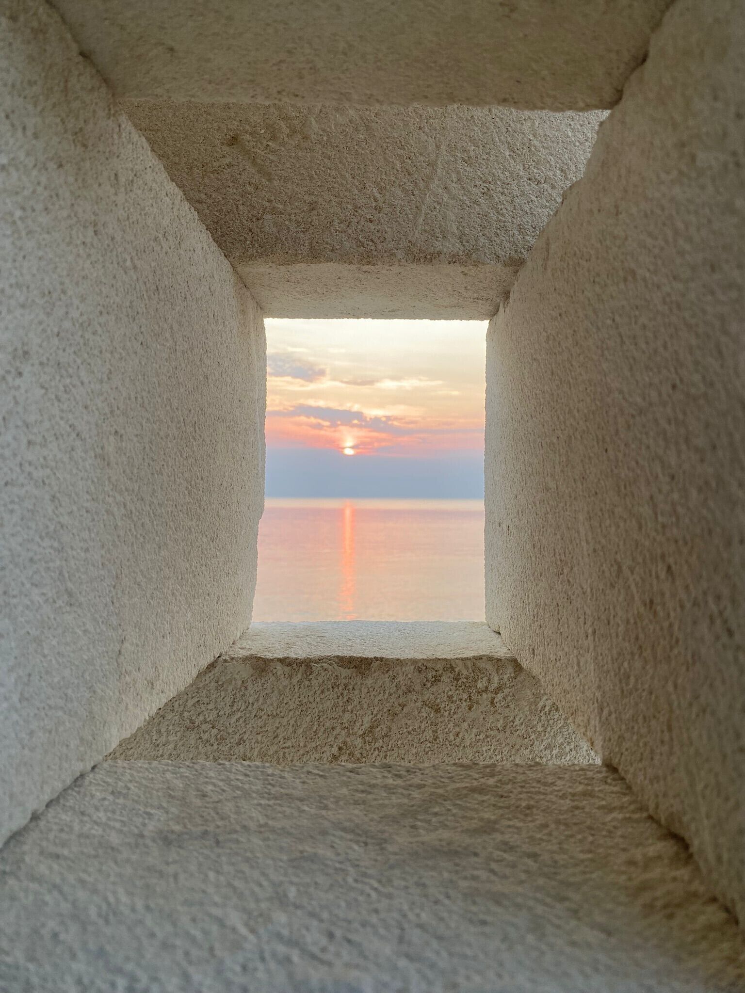 A square window with a view of a sunset over a calm body of water.