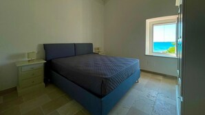 Ein Schlafzimmer mit einem Bett, einem Nachttisch, einem Fenster mit Blick und einem Deckenlüfter.