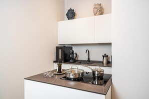 A modern kitchen with a gas stove, pots, a coffee maker, and decorative items on the countertop. - Stemma Apartment   Loggiato Verga (SIRACUSA)