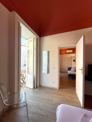 Ein Zimmer mit einem Bett, einem Sessel, einem Fernseher und einer Tür zu einem weiteren Raum.