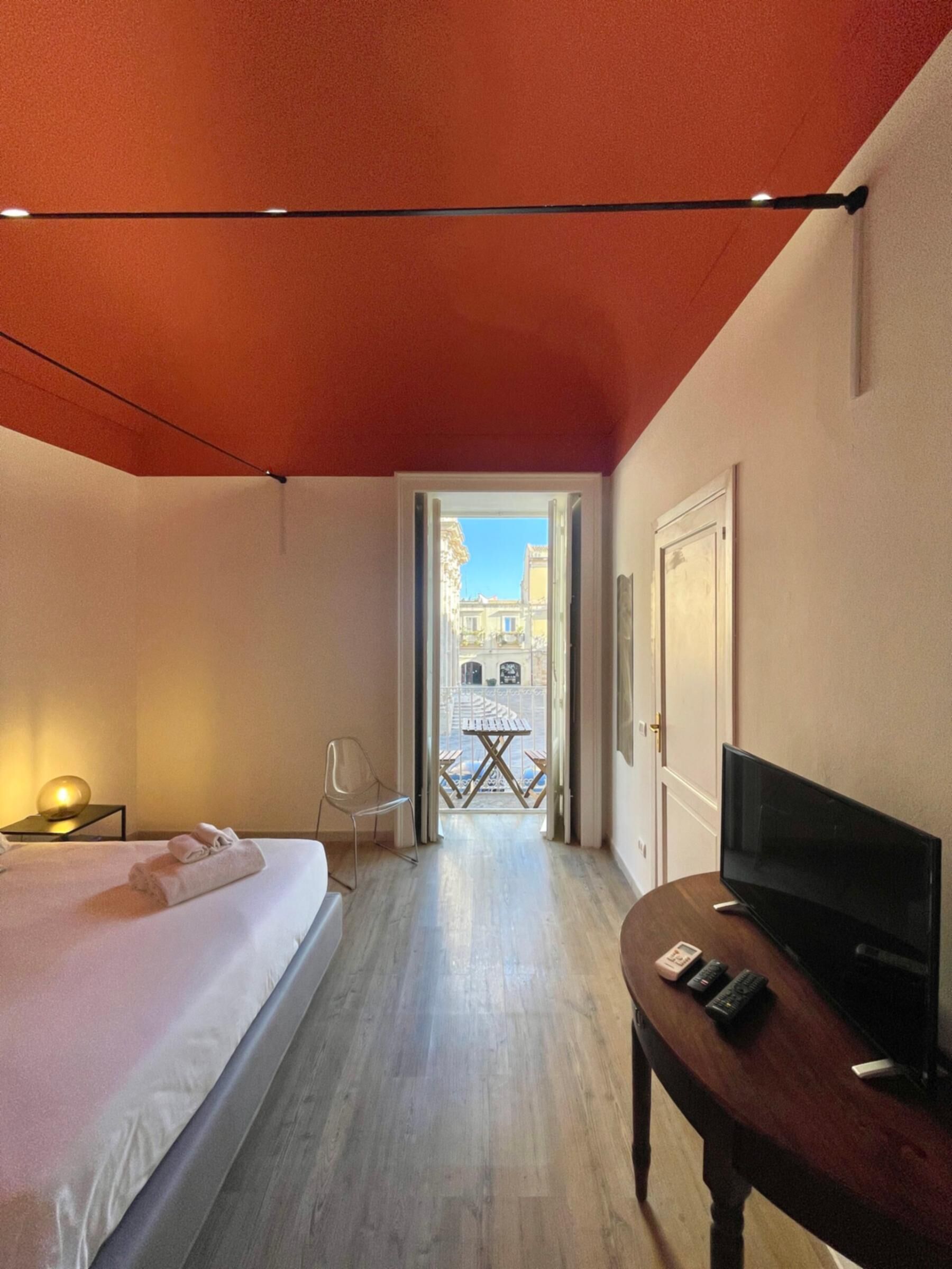 Una habitación de hotel con cama, televisor, escritorio y vista de la calle a través de una puerta abierta.