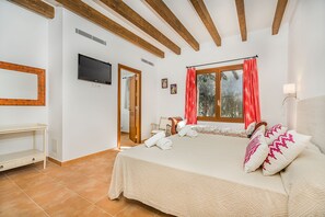 Ein Schlafzimmer mit einem großen Bett, einem Fernseher, einem Schreibtisch und einem Fenster mit Vorhängen.