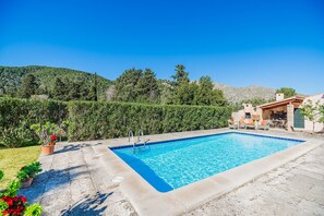 Ein rechteckiger Swimmingpool mit glatter, blauer Wasseroberfläche, umgeben von einer Steindeckfläche.