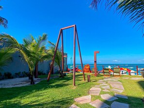 A beachside area with a swing set, palm trees, and a clear view of the ocean. - Smeralda Del Mare por Yolo (Ipojuca)