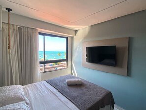 A hotel room with a bed, a TV mounted on the wall, and a window with a view of the ocean. - Smeralda Del Mare por Yolo (Ipojuca)