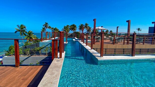 Une piscine avec une terrasse en bois, des palmiers et une vue sur l’océan.