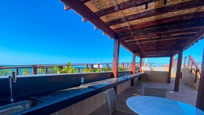 Un espace bar extérieur avec vue sur l’océan, une table ronde et des chaises en osier.