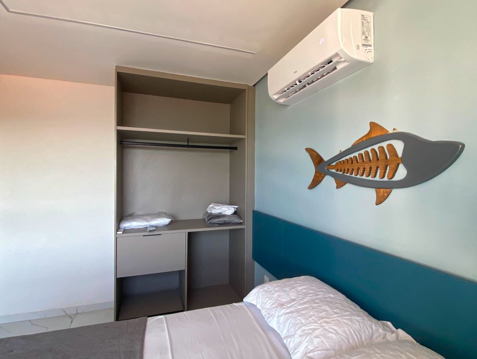 Quarto de hotel com cama, guarda-roupa, escrivaninha e ar condicionado.