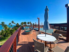 A deck with wicker furniture, a pool, and a view of the ocean. - Smeralda Del Mare por Yolo (Ipojuca)