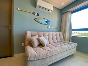 A room with a tufted sofa, a wall-mounted air conditioner, and a window with curtains. - Smeralda Del Mare por Yolo (Ipojuca)