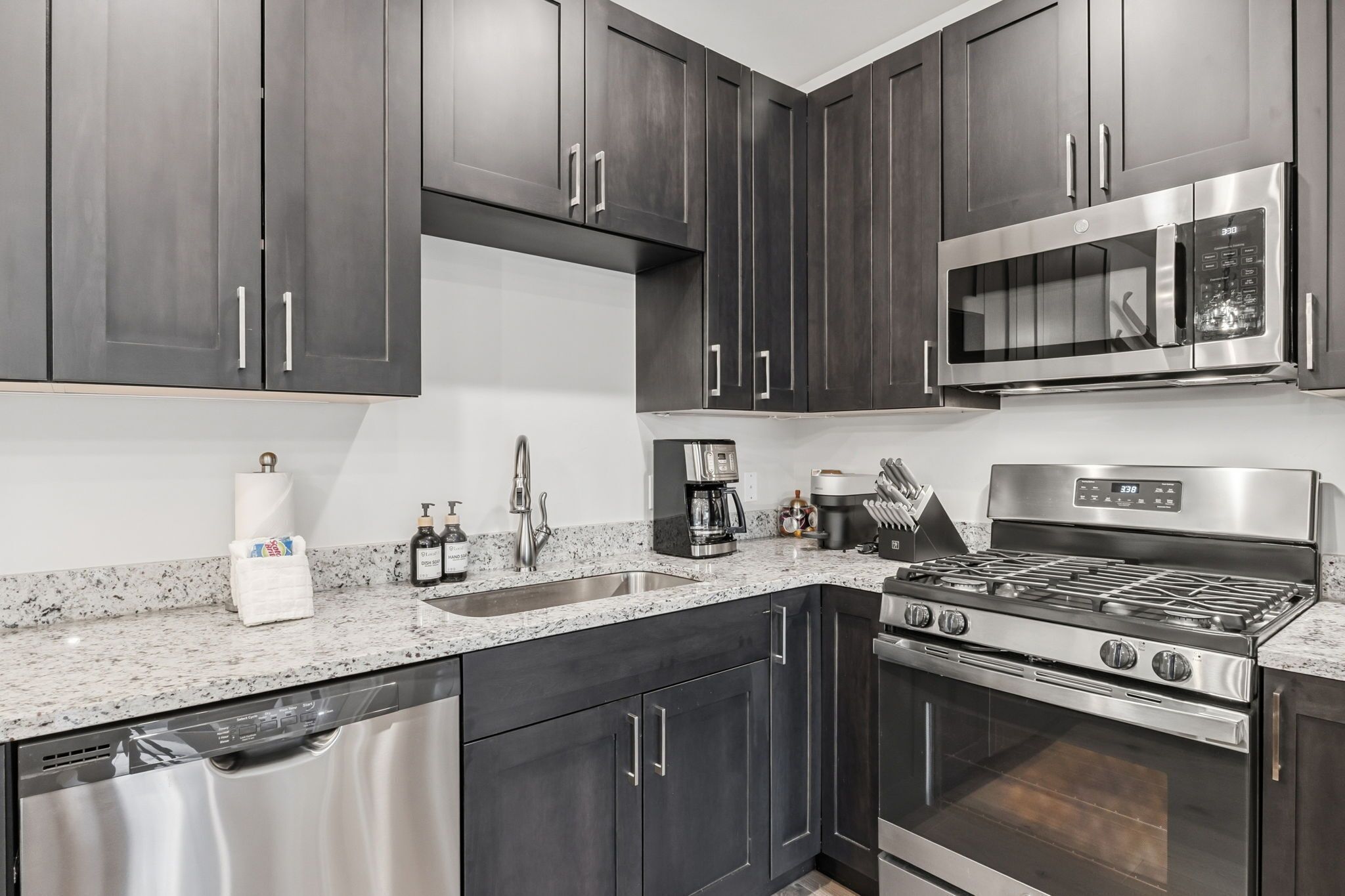 A modern kitchen with dark cabinets, stainless steel appliances, a granite countertop, and a dishwasher.