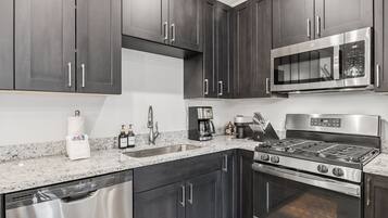 A modern kitchen with dark cabinets, stainless steel appliances, a granite countertop, and a dishwasher.