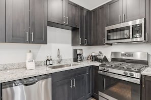 Una cocina moderna con armarios oscuros, electrodomésticos de acero inoxidable, encimera de granito y lavavajillas.
