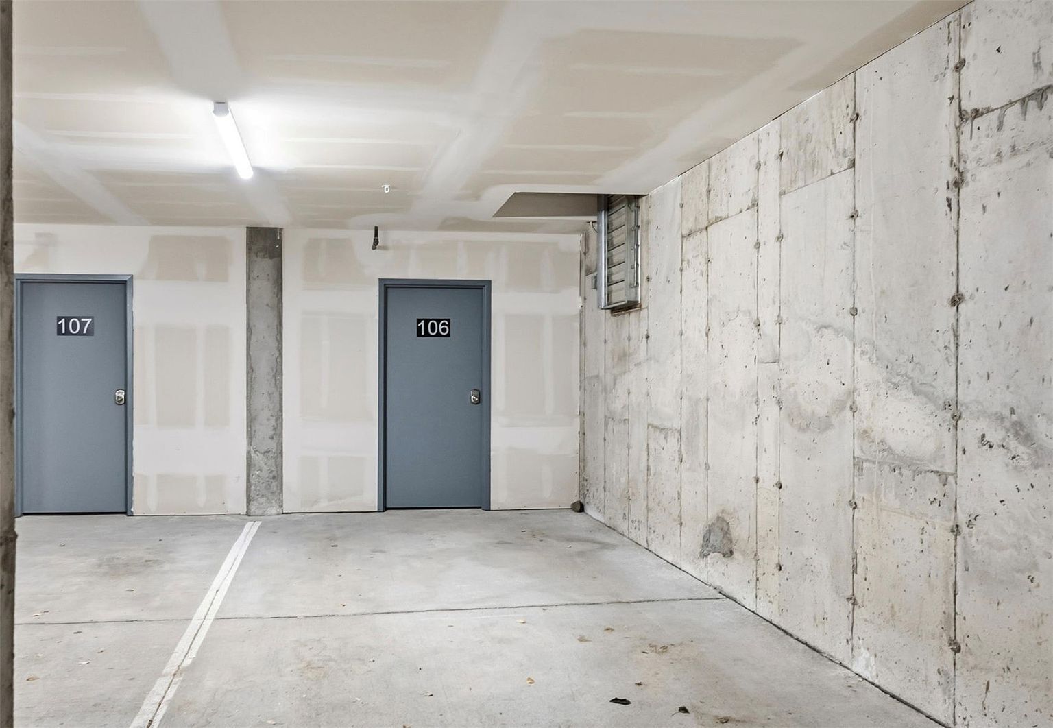 Un garaje con dos puertas, numeradas 107 y 106, y un muro de concreto.