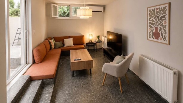 Una sala de estar con sofá, mesa de centro, televisor y una silla. Hay un radiador y una ventana con vistas al exterior.