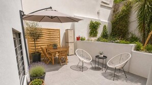 Un patio al aire libre con mesa y sillas de madera, un paraguas blanco y plantas en macetas.