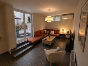 A modern living room with a sectional sofa, a coffee table, a white armchair, and a dining area with a table and chairs. - Boutique 2Bd Oasis in Lycabettus with Garden Patio (Athina)