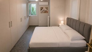 Un dormitorio con cama, mesita de noche, ventana y aire acondicionado de pared.