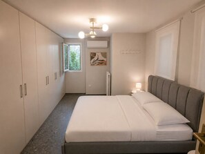 A bedroom with a bed, a nightstand, a window, and a wall-mounted air conditioner. - Boutique 2Bd Oasis in Lycabettus with Garden Patio (Athina)