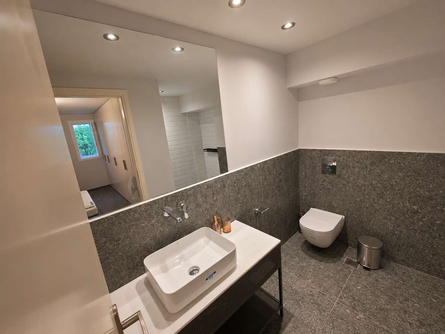 Ein modernes Badezimmer mit einem großen Spiegel, einem weißen Waschbecken, einem Bidet und einer Toilette.