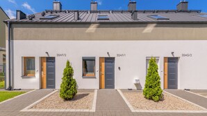 Ein modernes Gebäude mit nummerierten Türen, einer flachen Dachterrasse und zwei kleinen Bäumen davor.