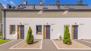 A modern building with numbered doors, a flat roof, and two small trees in front. - Apartamenty Sun & Snow LEMON (Władysławowo)