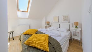 A bedroom with a sloped ceiling, a skylight, a bed with white linens, two bedside tables with lamps, and artwork on the wall. - Apartamenty Sun & Snow LEMON (Władysławowo)