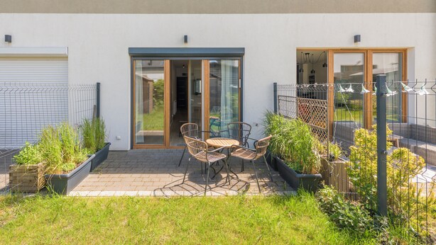 Eine Terrasse mit Tisch und Stühlen, eine Schiebetür und ein eingezäunter Gartenbereich.