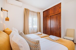 A hotel room with two beds, a wooden wardrobe, a chair, and a hanging light fixture. - Villa Sousa by Dreamplaces (Albufeira)